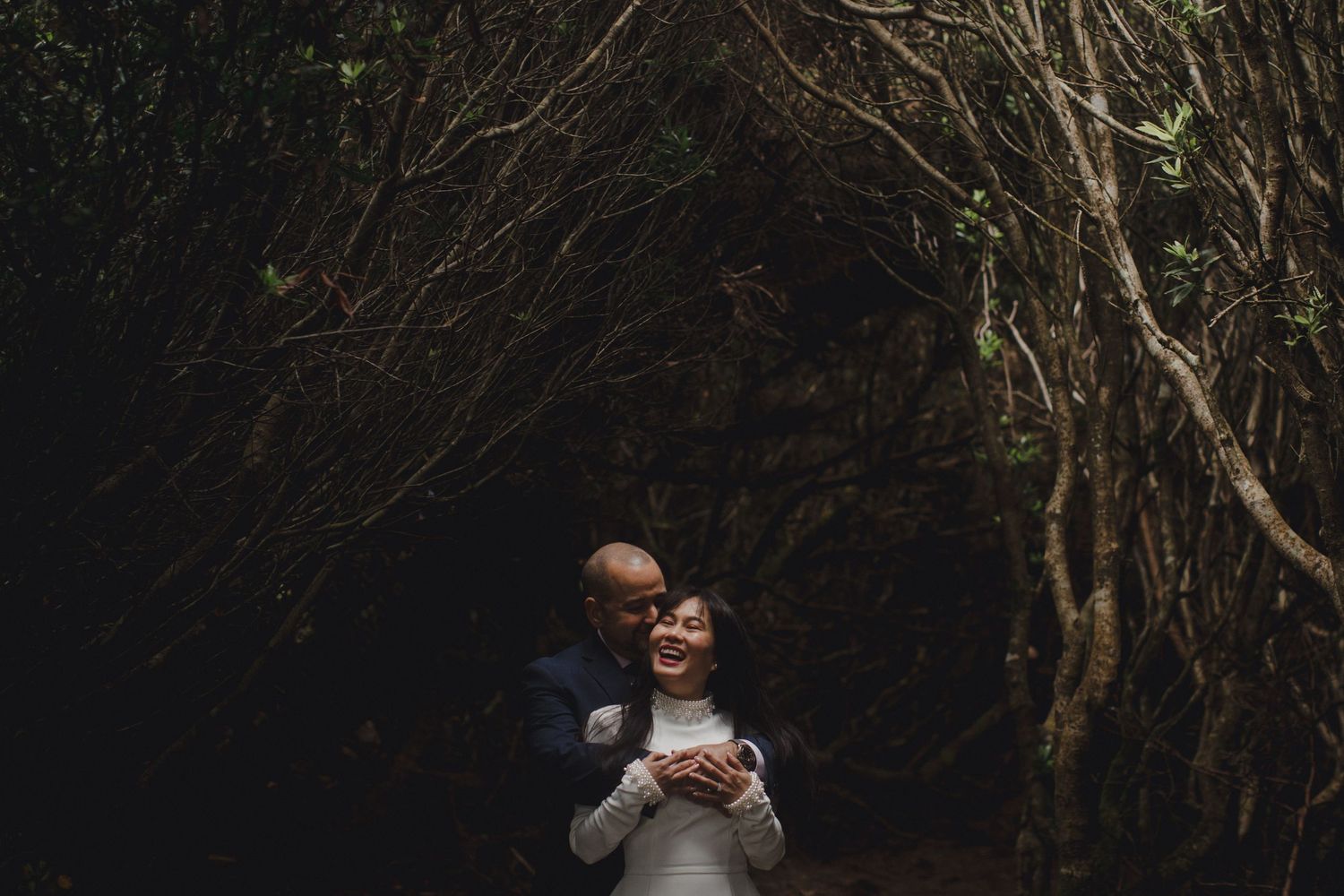 Couple embracing romantically in a dark enchanting forest tunnel of trees.