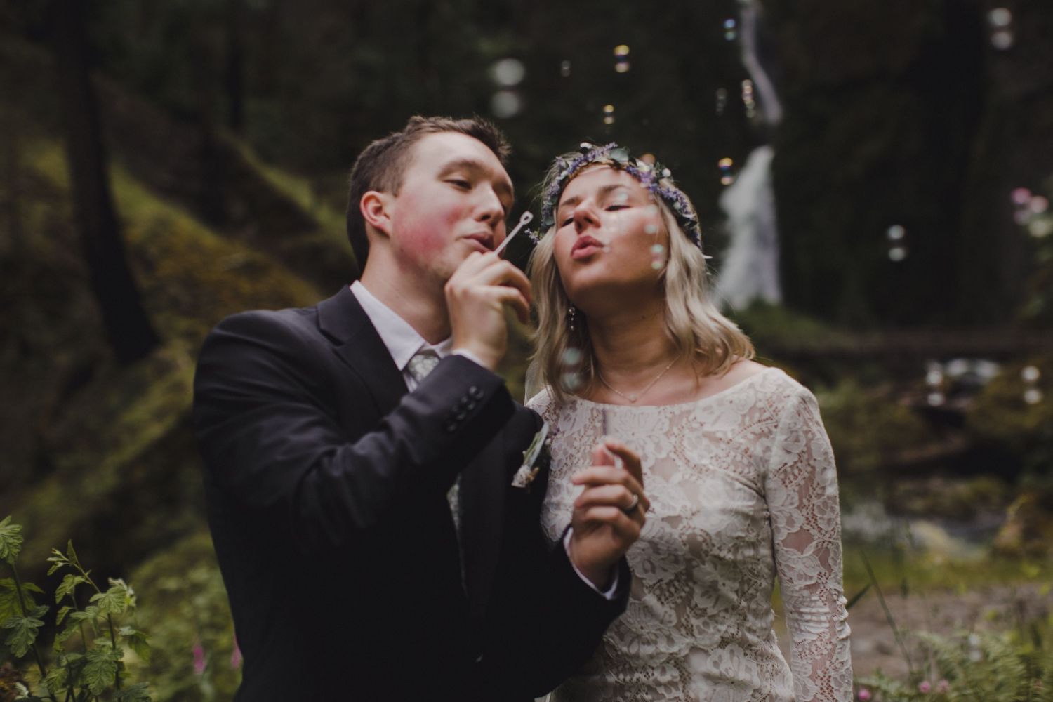 A romantic moment captured as newlyweds blow dandelions together in a misty forest setting.