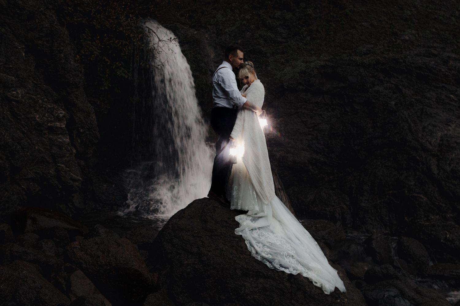 Romantic wedding portrait in front of misty waterfall with long white dress.