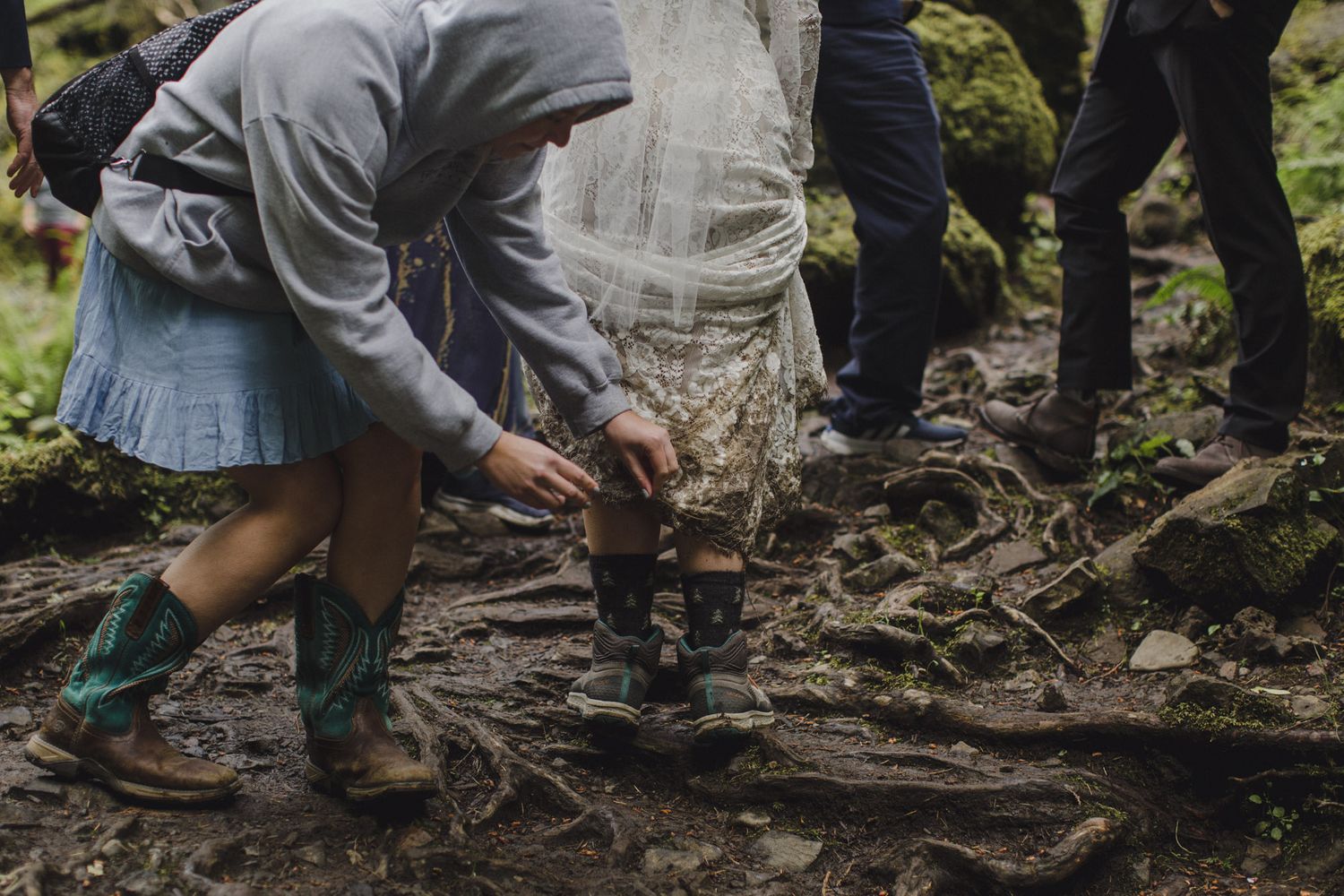 Someone in rubber boots bends down to adjust details near mossy tree roots.