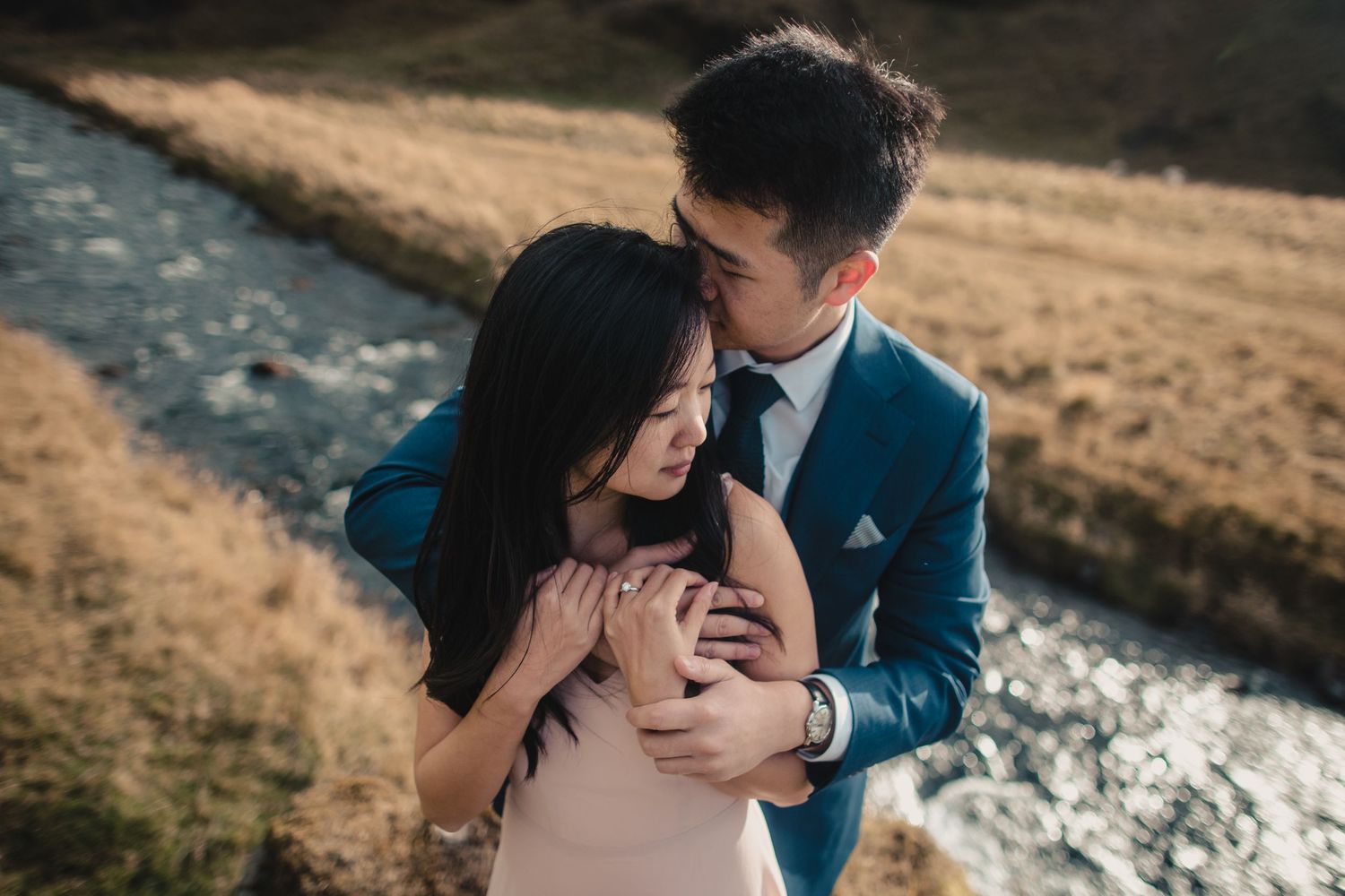 Intimate moment shared between couple near flowing river in mountain setting.