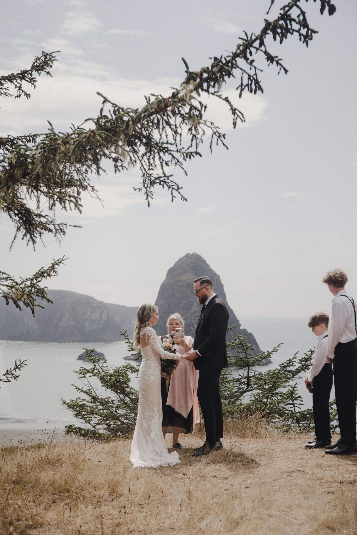 Couple exchanges vows at coastal elopement with Haystack Rock backdrop, children present, on Oregon's scenic cliffside.