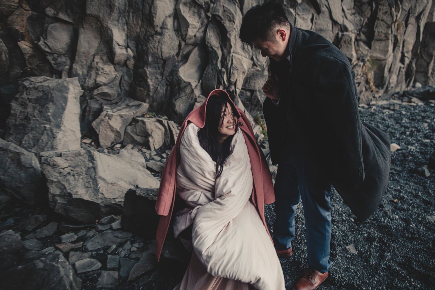 A romantic scene against rocky cliffs with flowing white dress and warm outerwear.