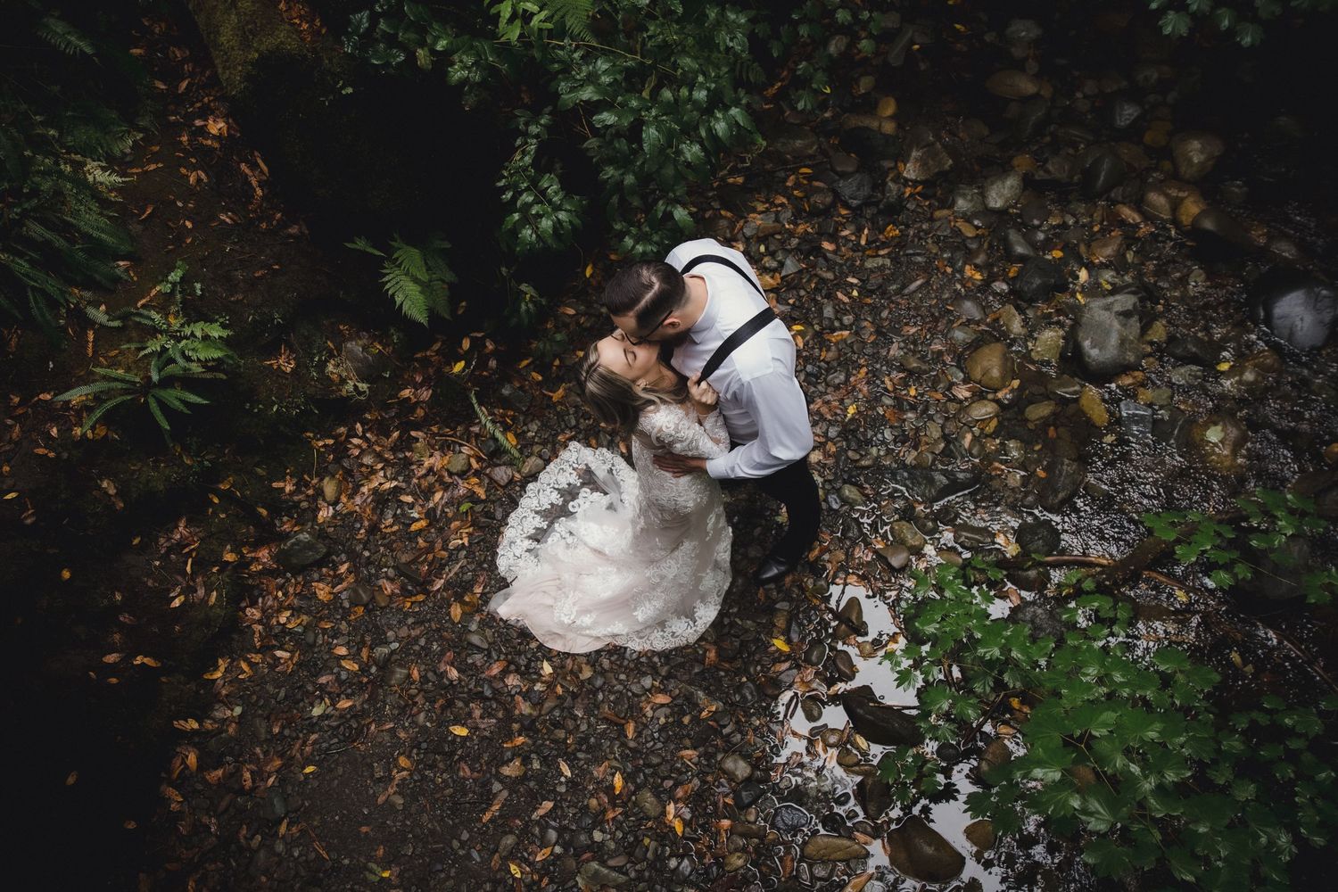 Aerial view of bride and groom embracing on a rocky creek bed surrounded by autumn leaves.