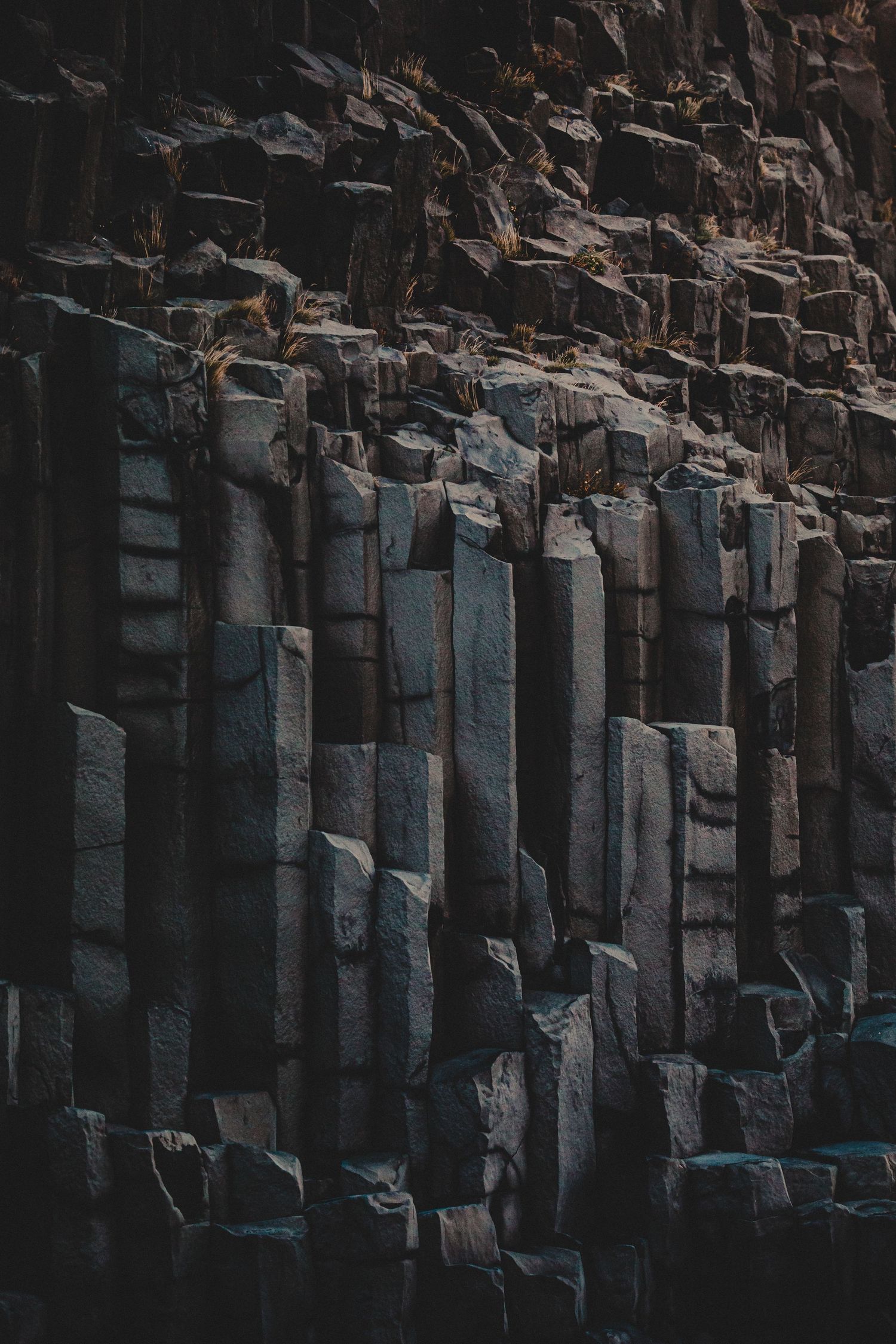 Dramatic columnar basalt rock formations create geometric patterns in dark moody lighting.