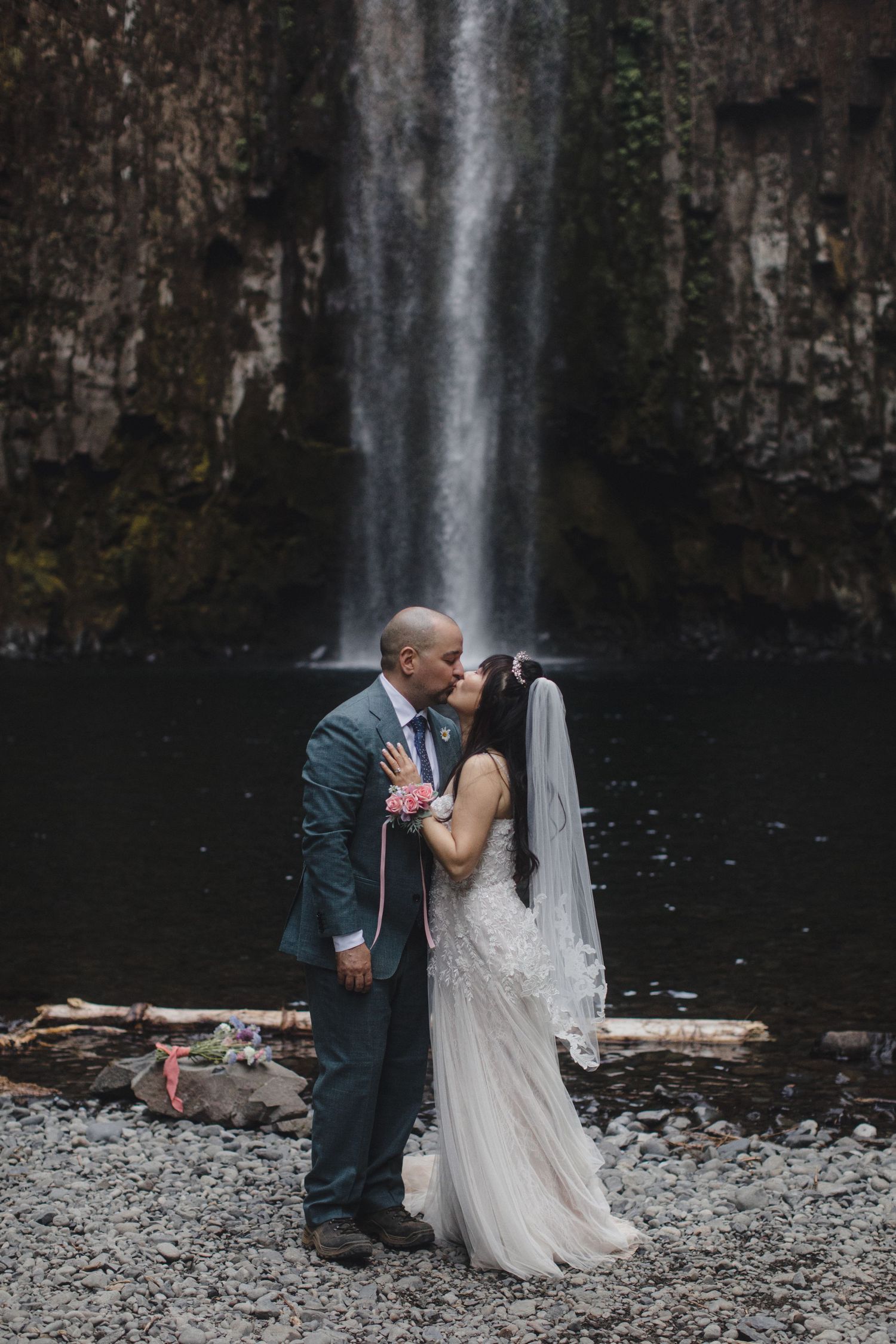 Bride and groom sharing a kiss in front of a stunning waterfall backdrop.