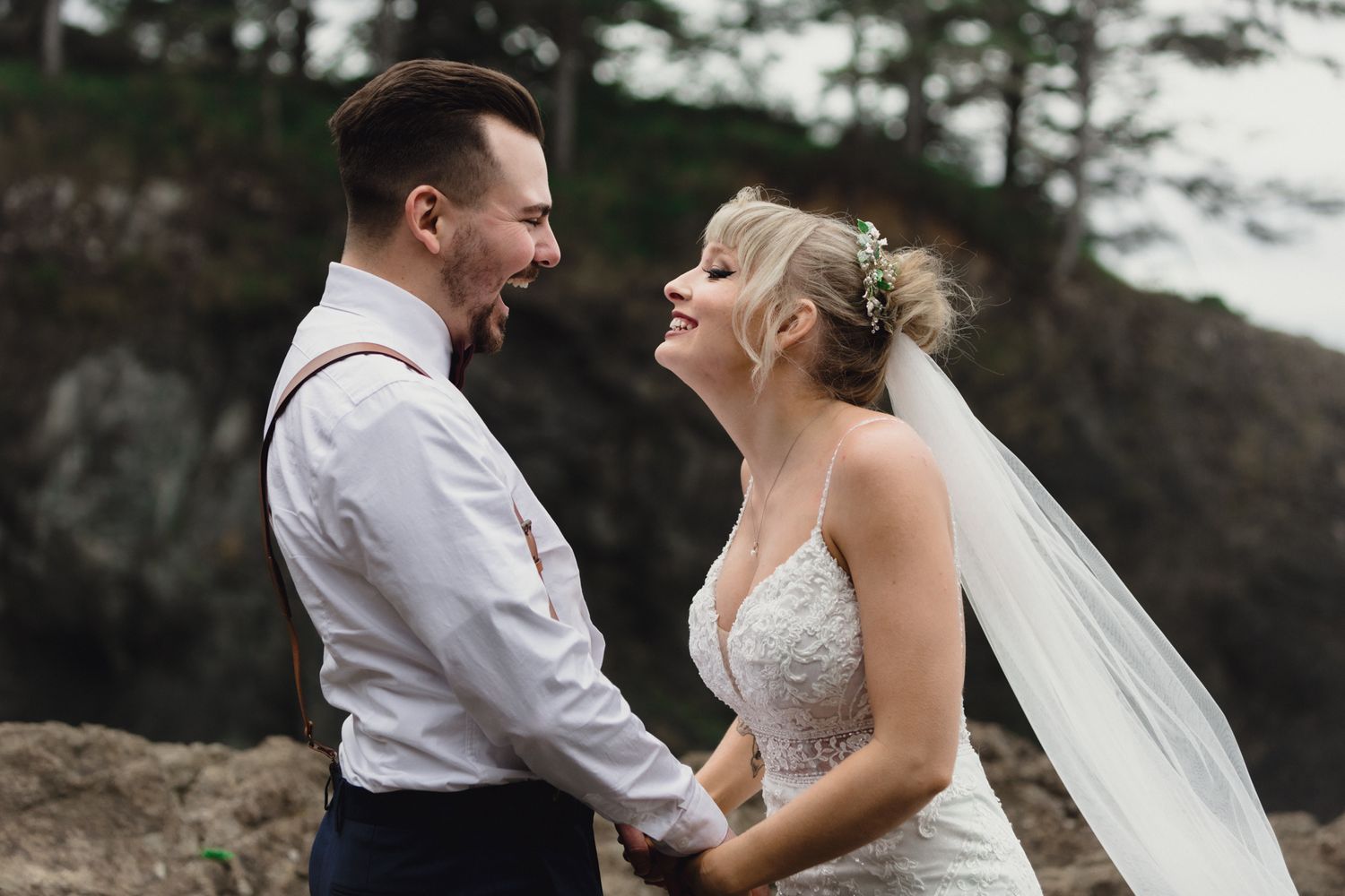 A candid moment of shared joy between newlyweds on rocky coastal cliffs.