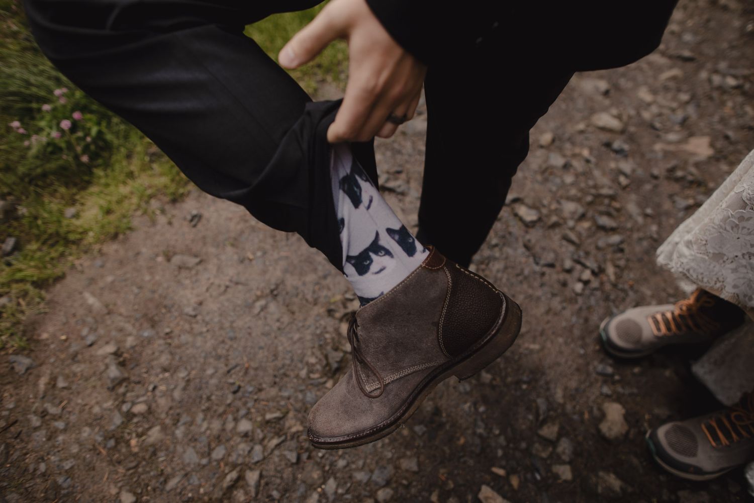 Close-up of brown leather boots and patterned socks being adjusted on a dirt path.