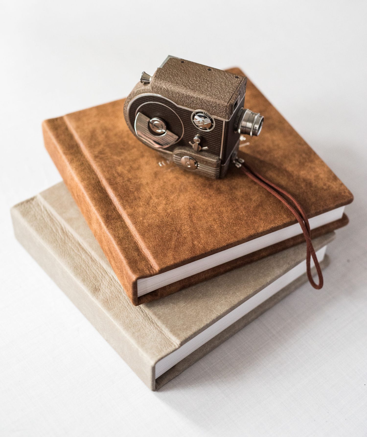 Vintage miniature film camera resting on two stacked leather-bound journals on a white surface.