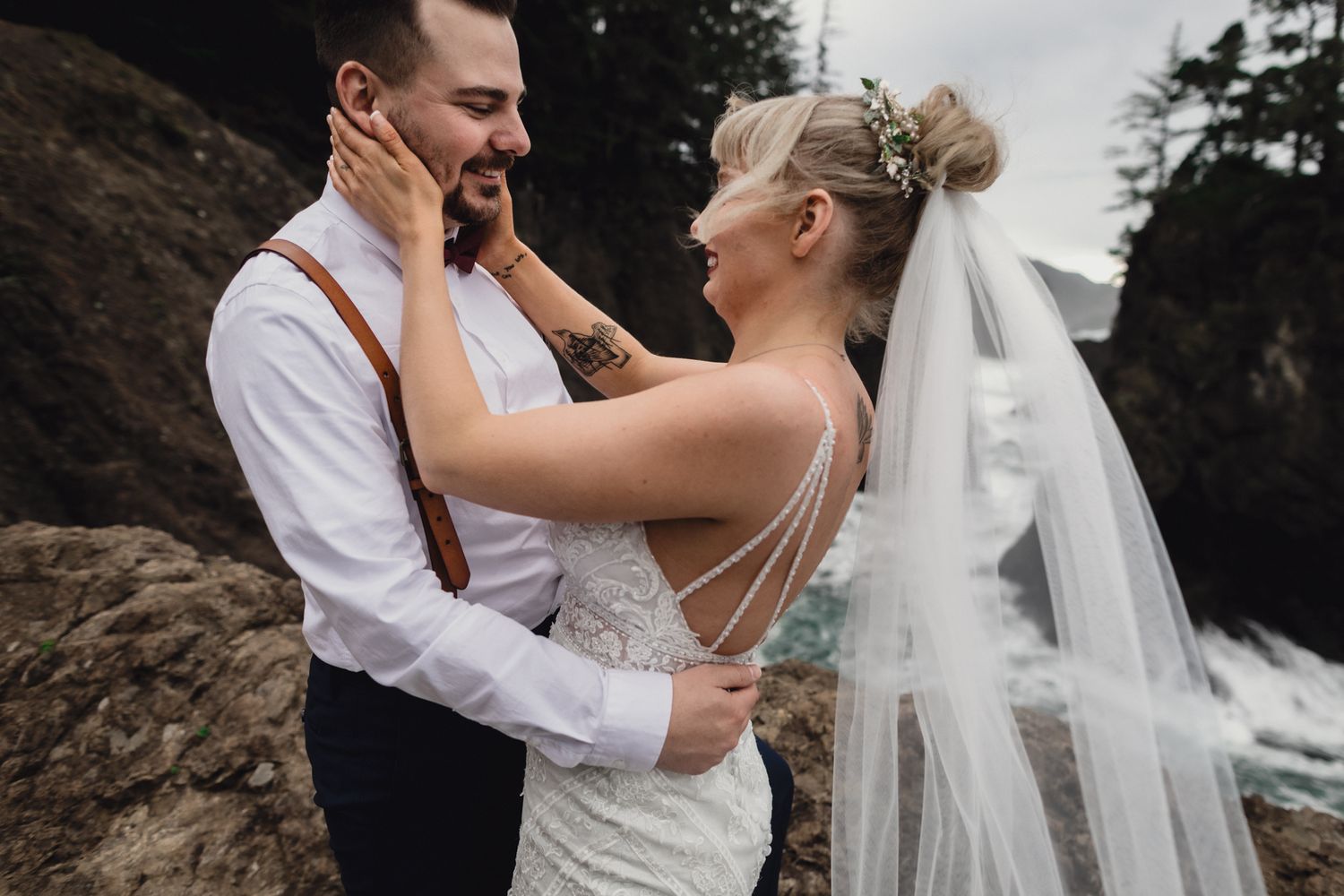 A tender moment shared on a cliffside with flowing white veil catching the wind.