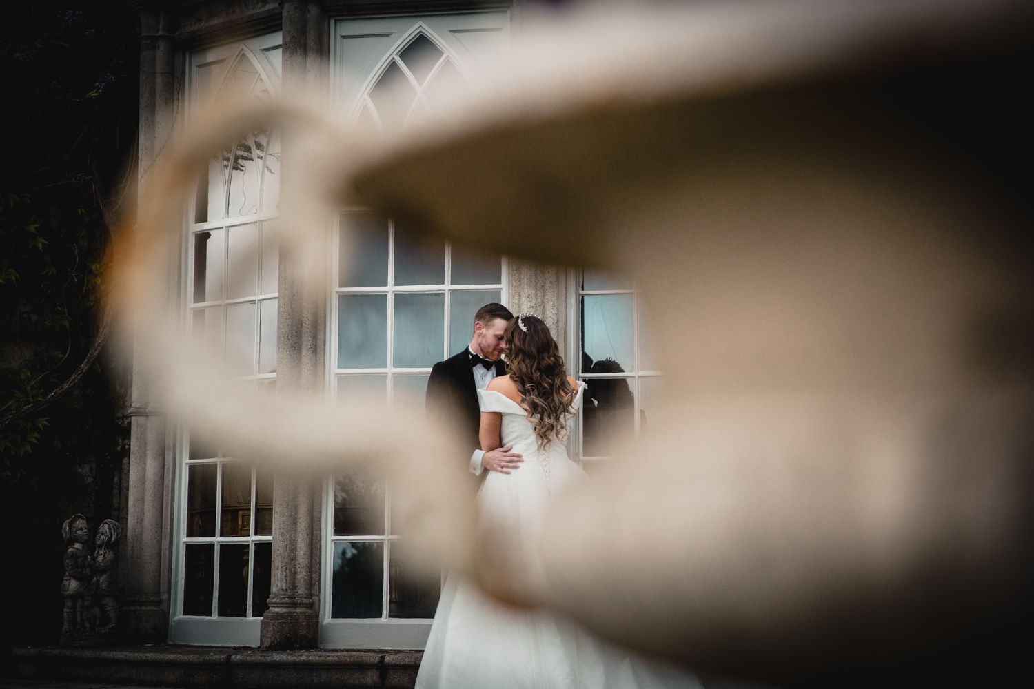 An artistic wedding portrait framed through blurred foreground elements.
