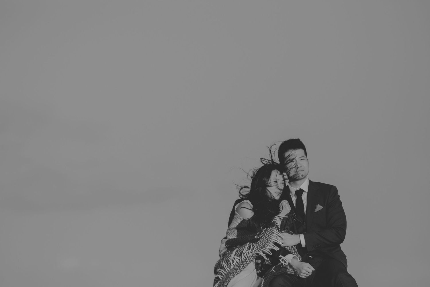 A black and white intimate portrait captured against a minimalist sky background.