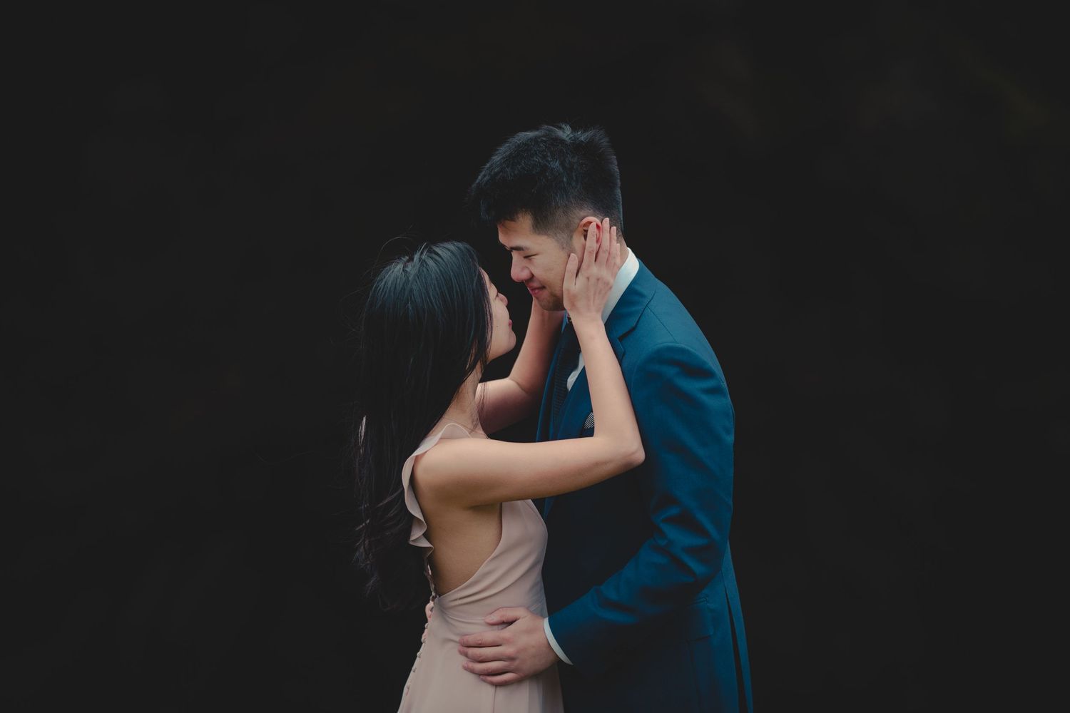 Intimate portrait of couple embracing against dark background in formal attire.