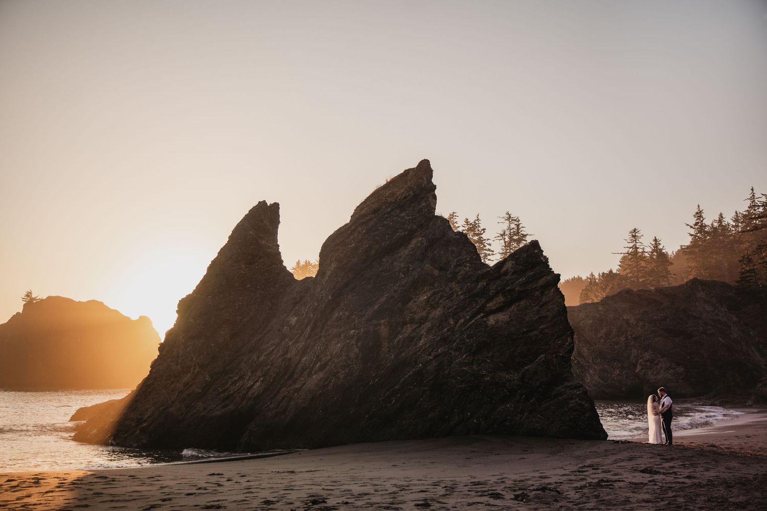 Couple eloping at sunset on a rocky Pacific Northwest beach with dramatic sea stacks and golden light.