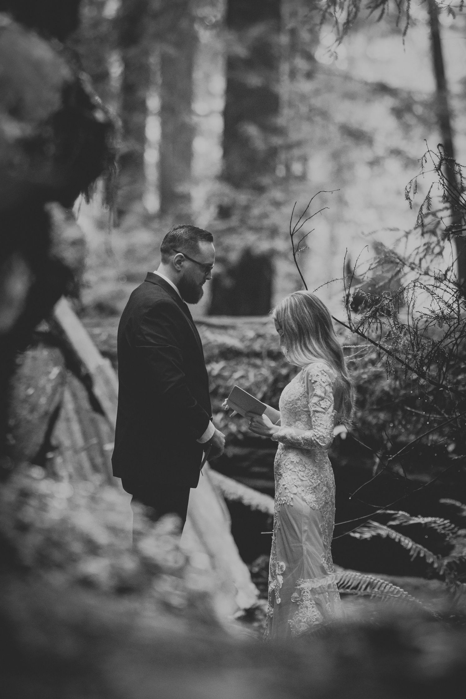Black and white photo of bride and groom exchanging vows in a misty forest during intimate elopement.