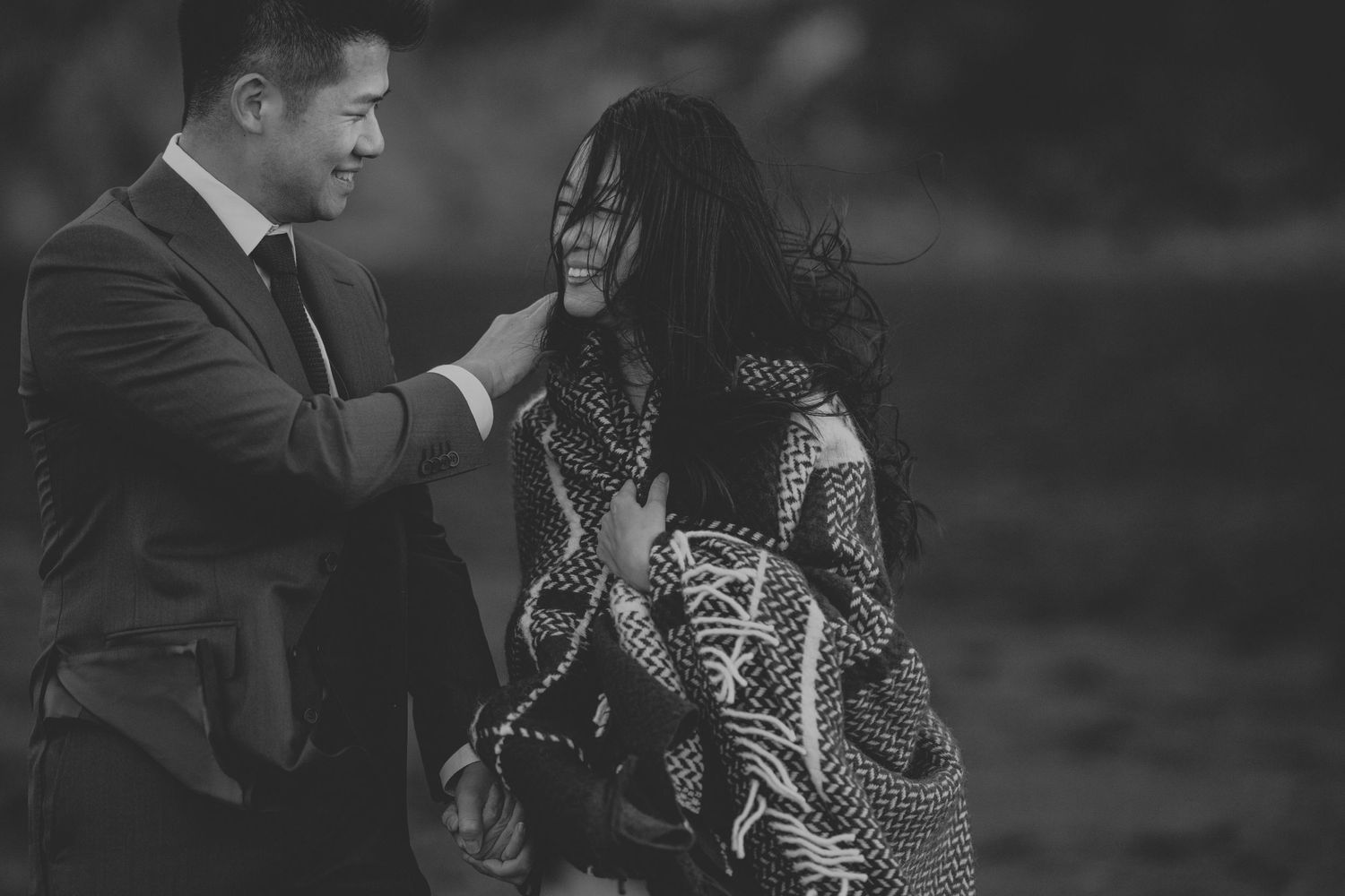 A black and white portrait of a couple sharing an intimate moment on a windswept coast.
