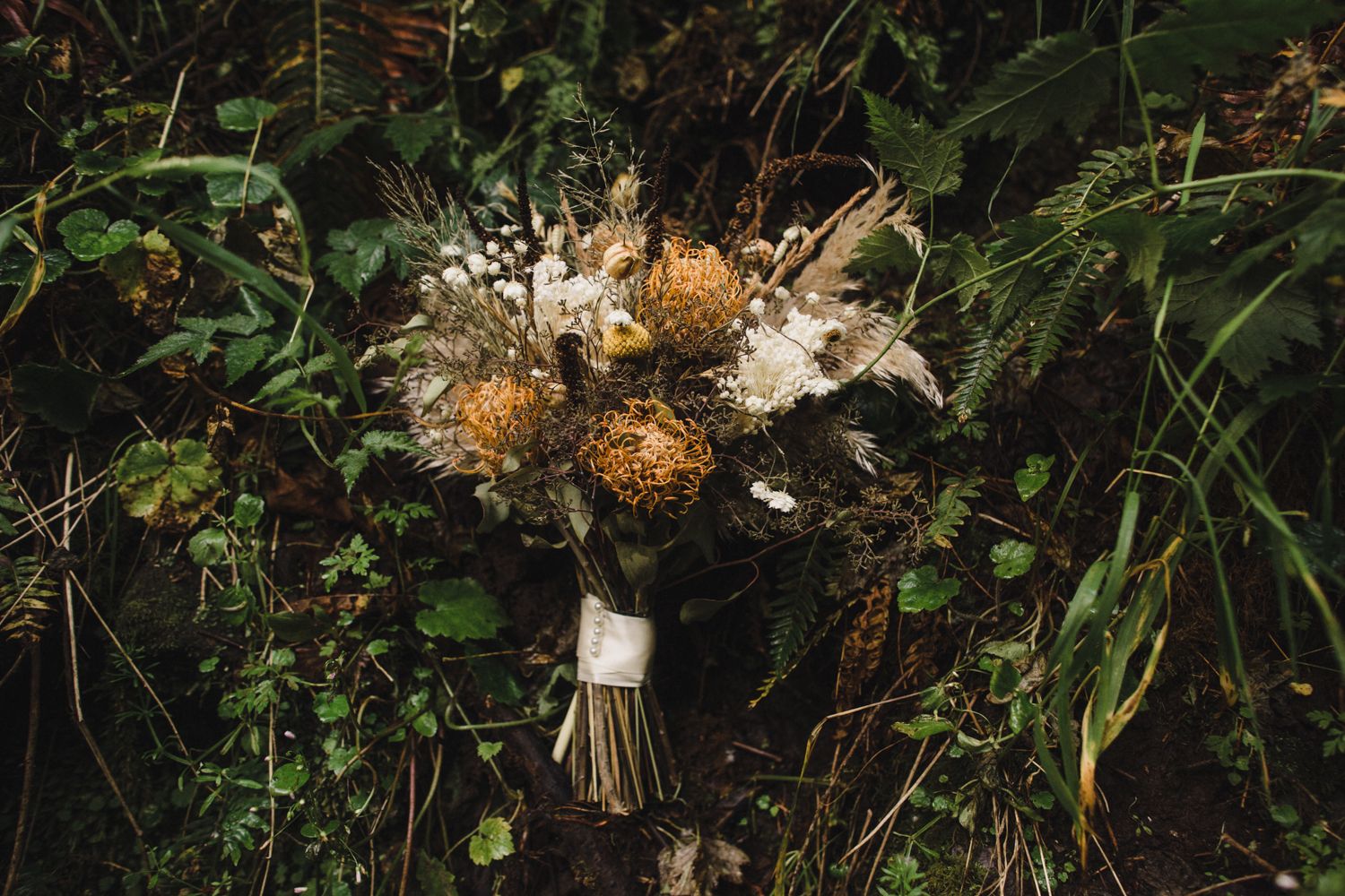 A rustic wedding bouquet with dried flowers and white blooms against a dark natural background.