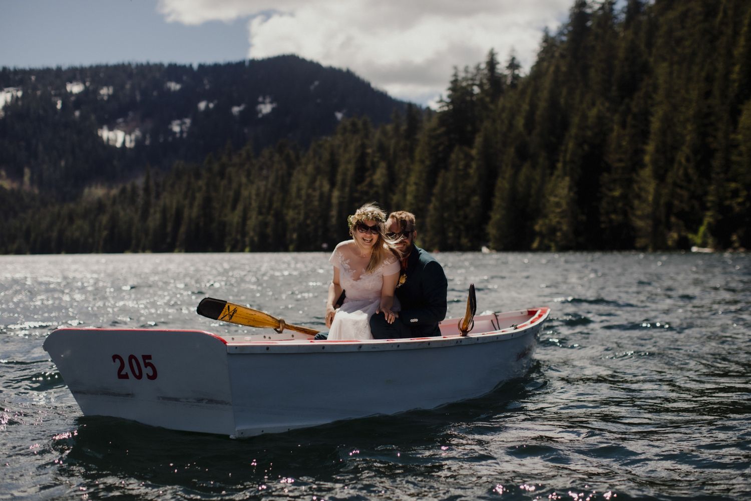Couple sitting together in small white numbered boat on scenic mountain lake.