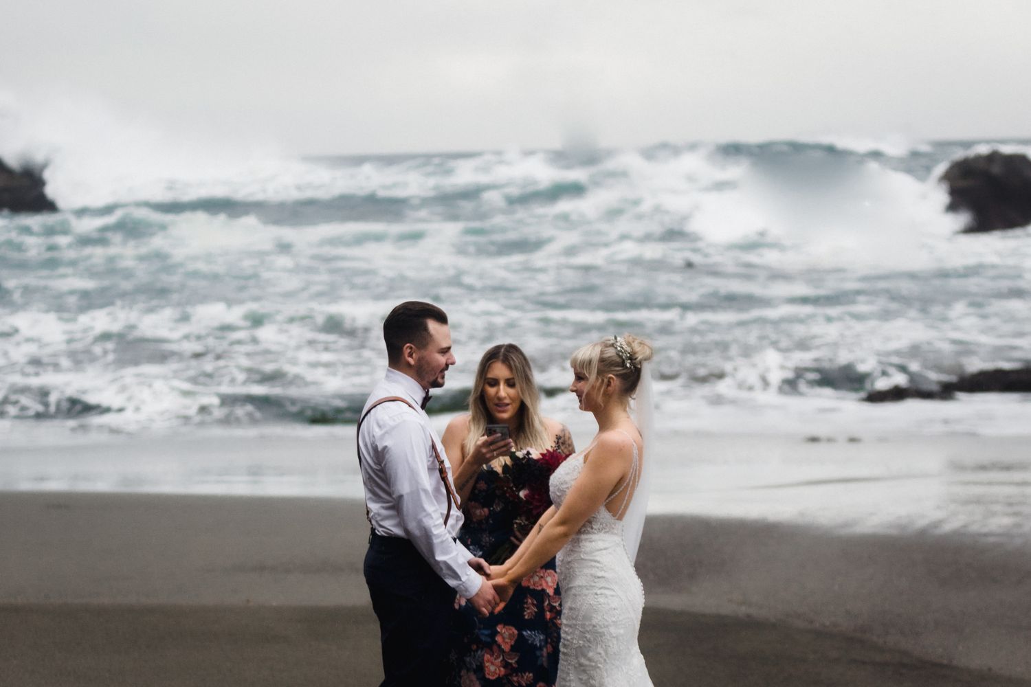 An intimate beach wedding ceremony with crashing waves and dark cliffs in the background.