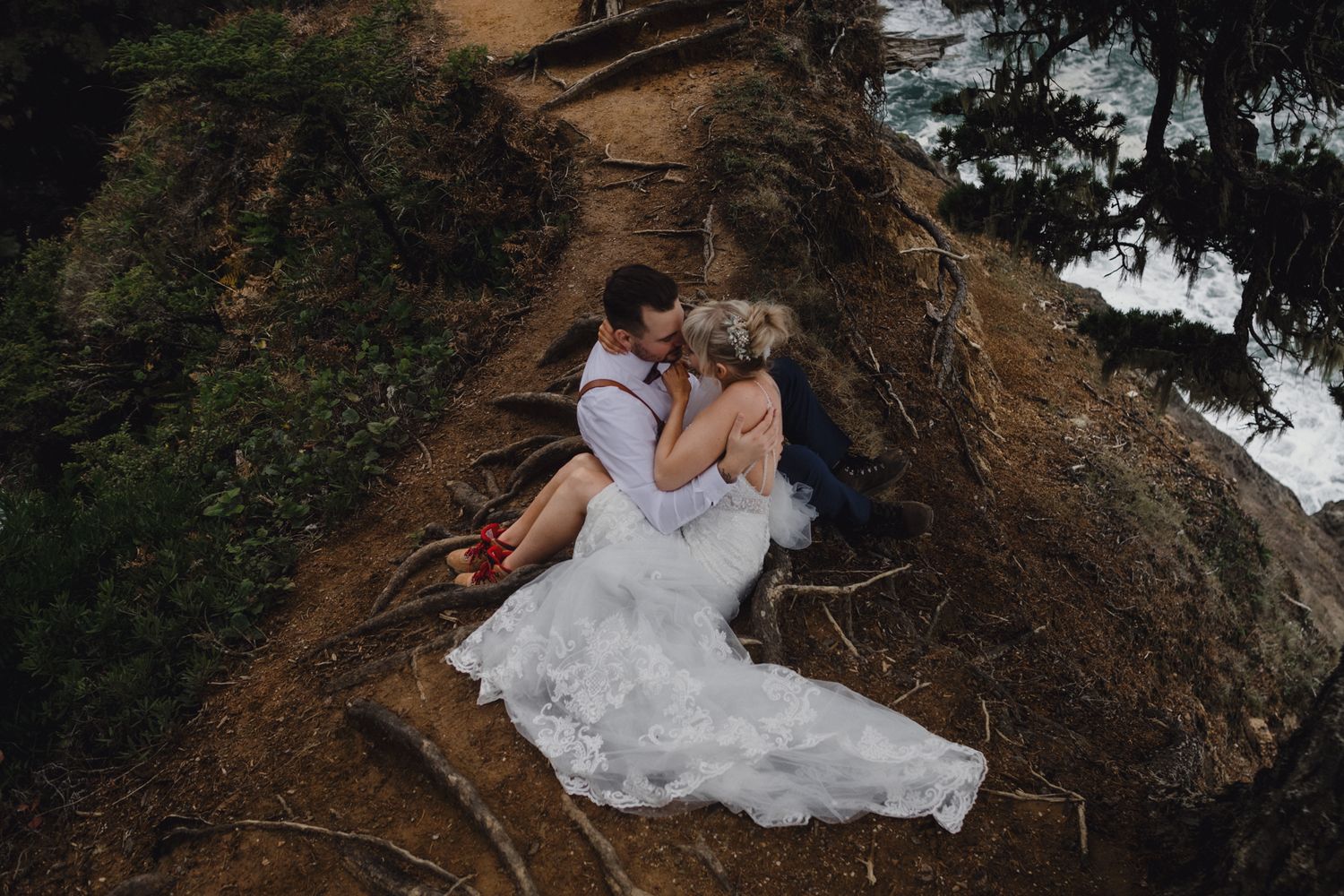 A romantic wedding moment captured on a rugged cliff edge overlooking the Pacific coast.