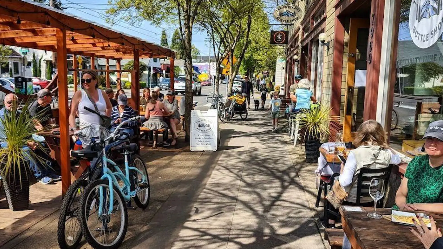 A busy neighborhood street in Portland Oregon where people sit at cafes, ride bikes, and enjoy a beautiful spring day.