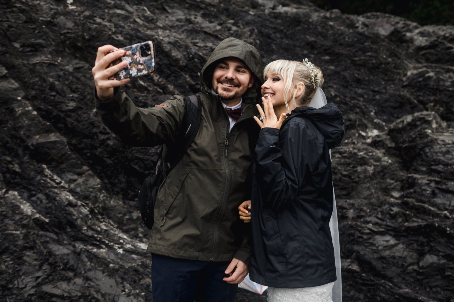 Two adventurers taking a fun selfie against dramatic rocky cliffs in outdoor winter gear.