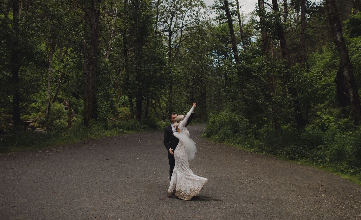 A romantic dance moment captured on a woodland trail beneath towering trees.