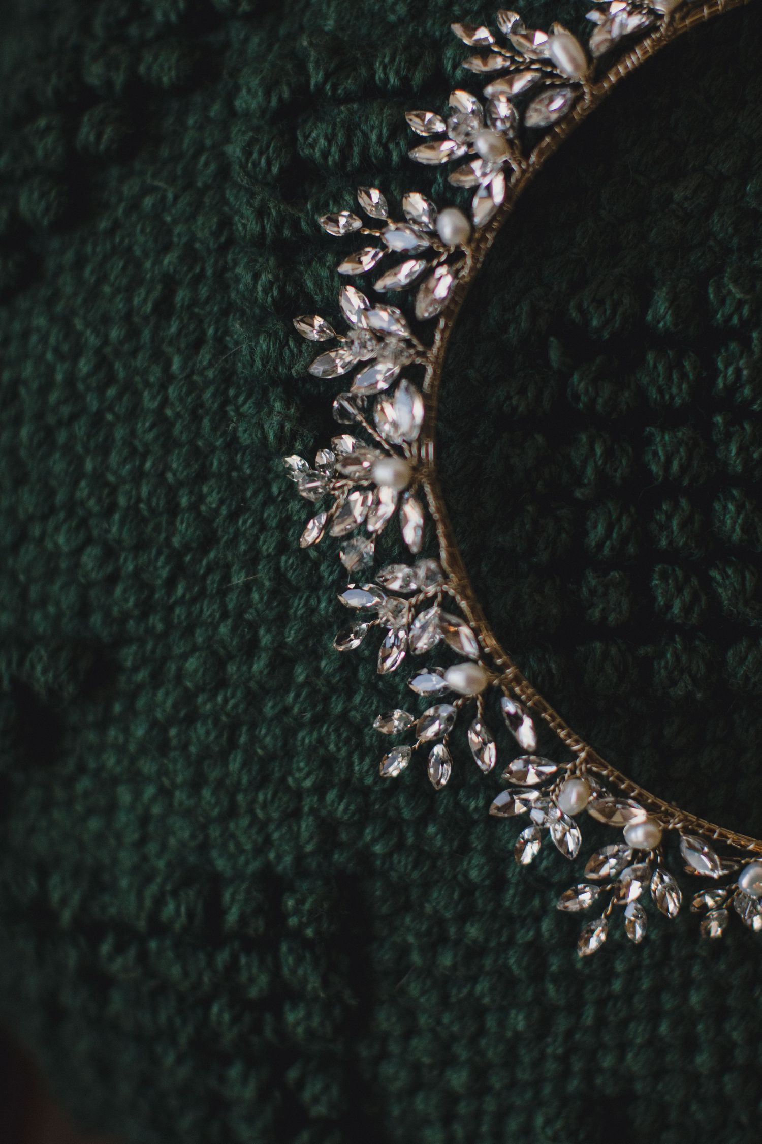 Elegant crystal and pearl bridal hair crown on dark green knit fabric.