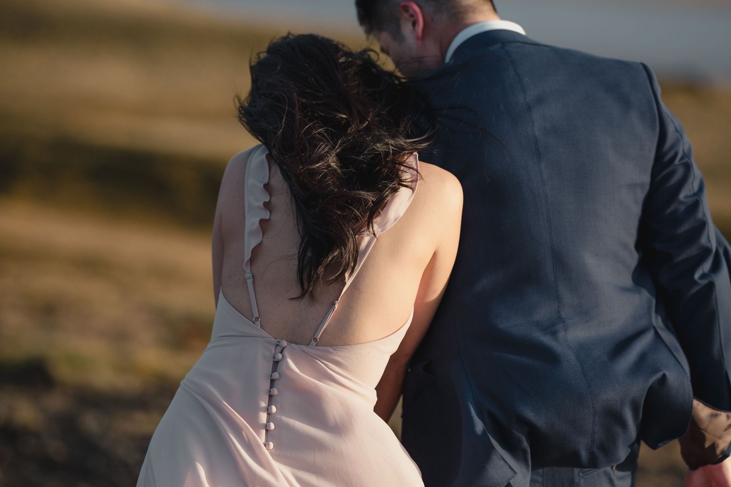 A candid moment captured of a couple in formal wear walking on coastal terrain.