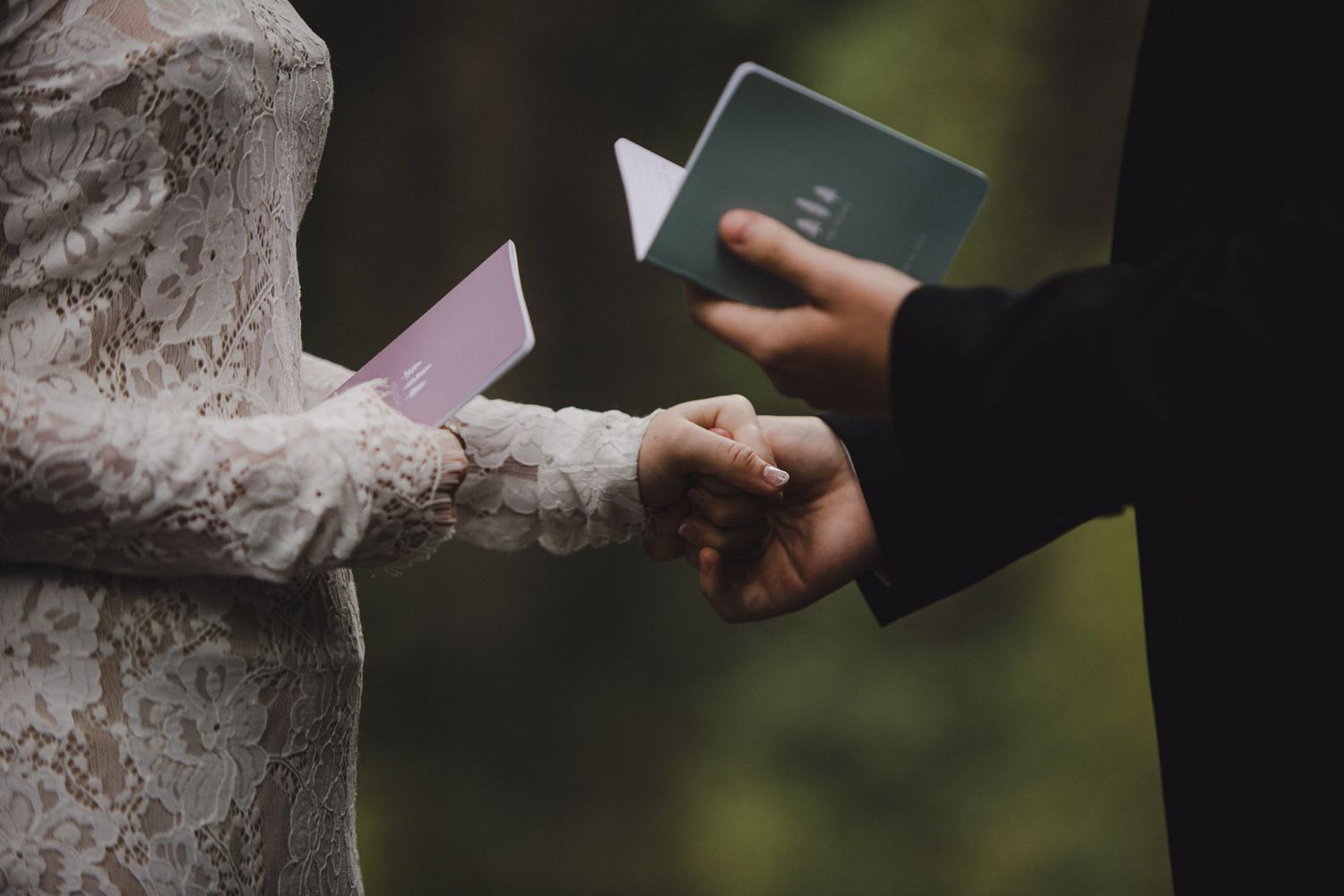 Closeup of hands exchanging vows during outdoor wedding ceremony.