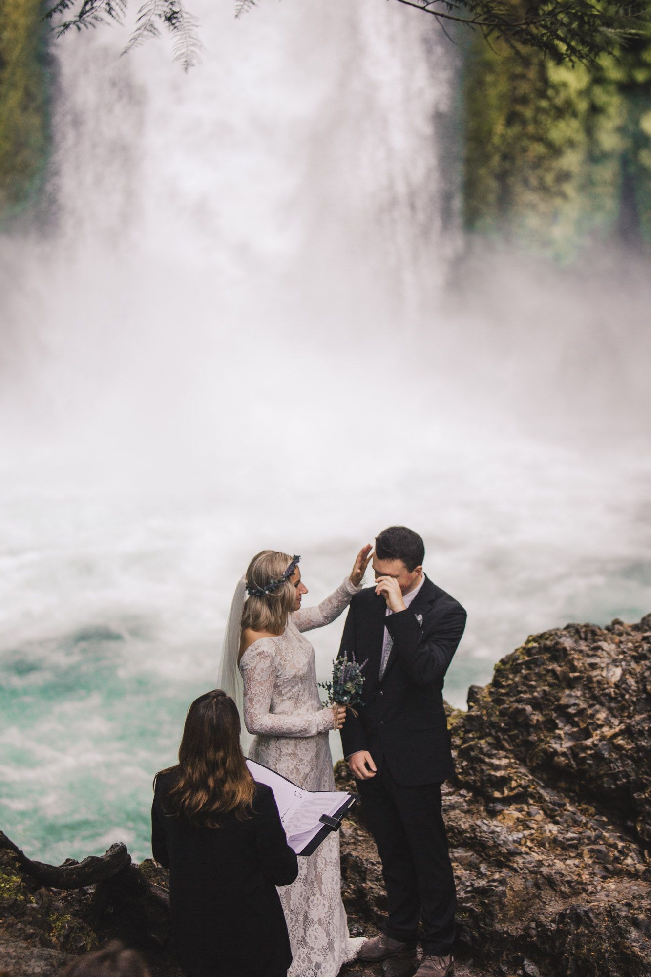An intimate wedding ceremony unfolds beside a majestic waterfall with mist and turquoise waters.