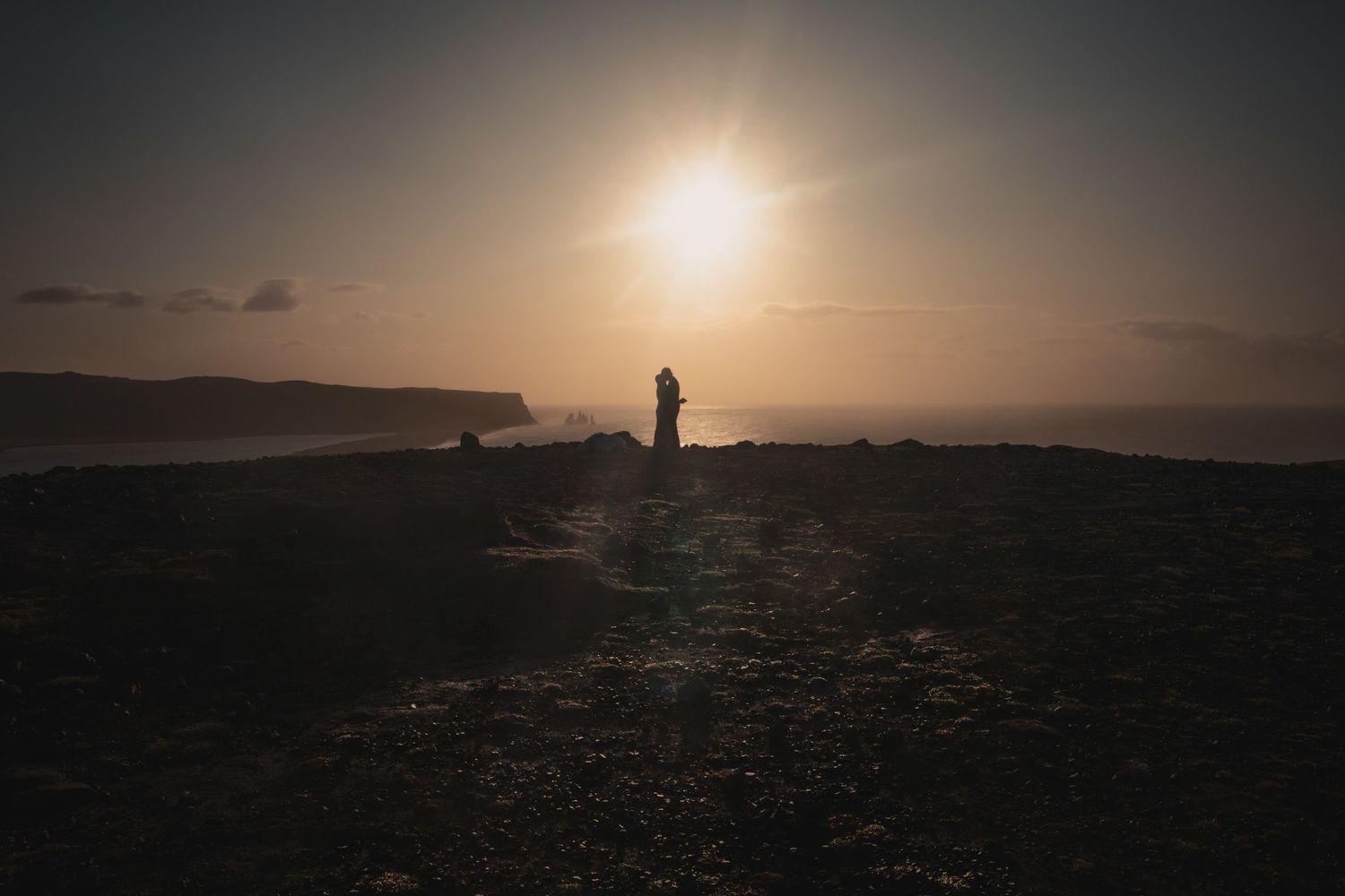 Silhouette of figures against golden sunset on coastal cliffs.