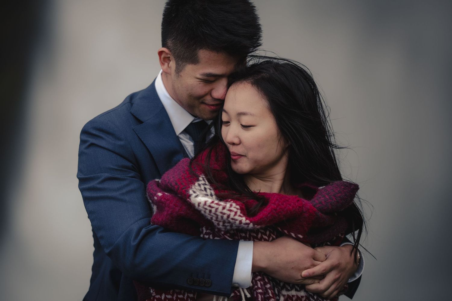 Intimate winter portrait of couple embracing while wrapped in burgundy scarf.