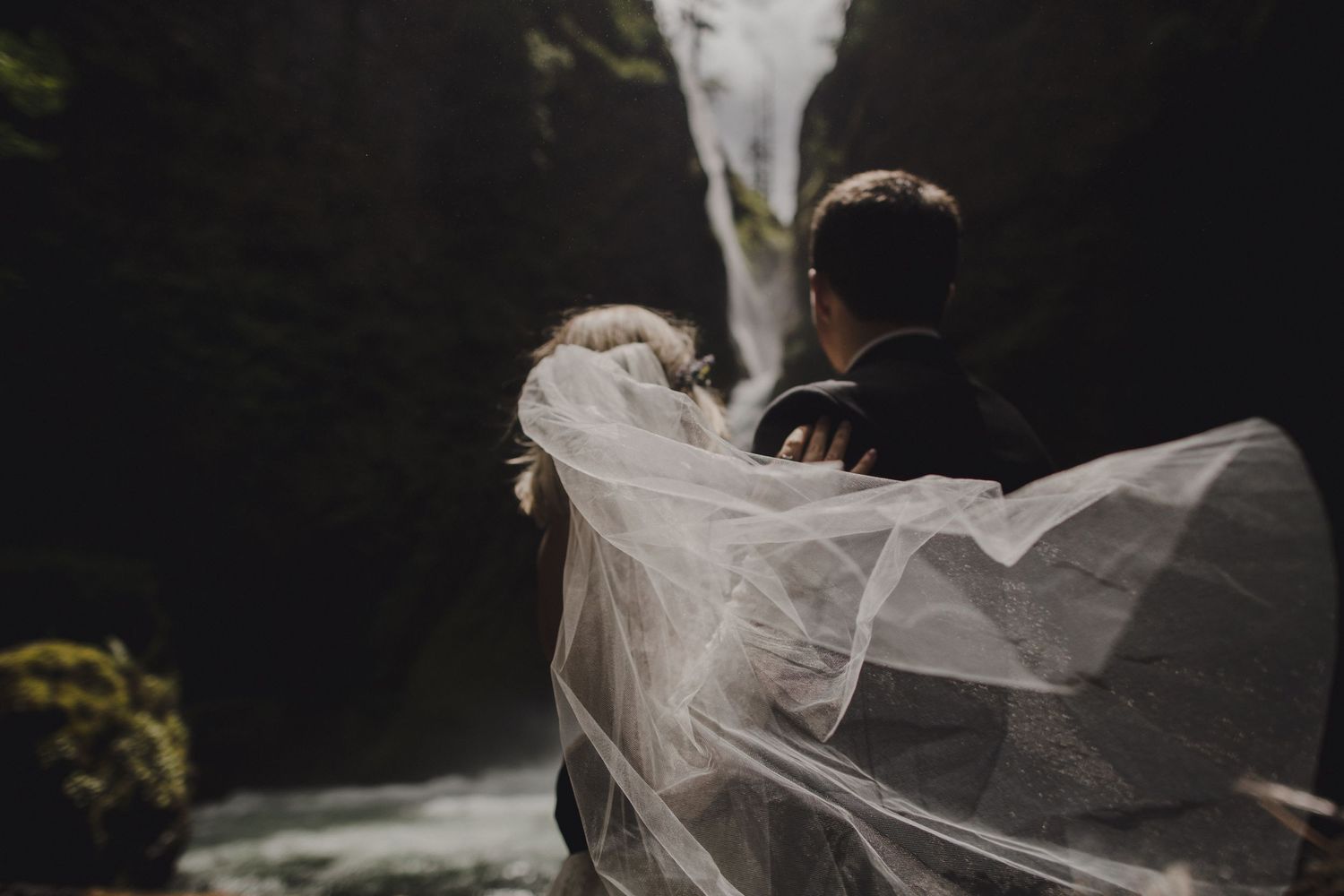 A flowing veil catches the wind as a waterfall rushes in the background.
