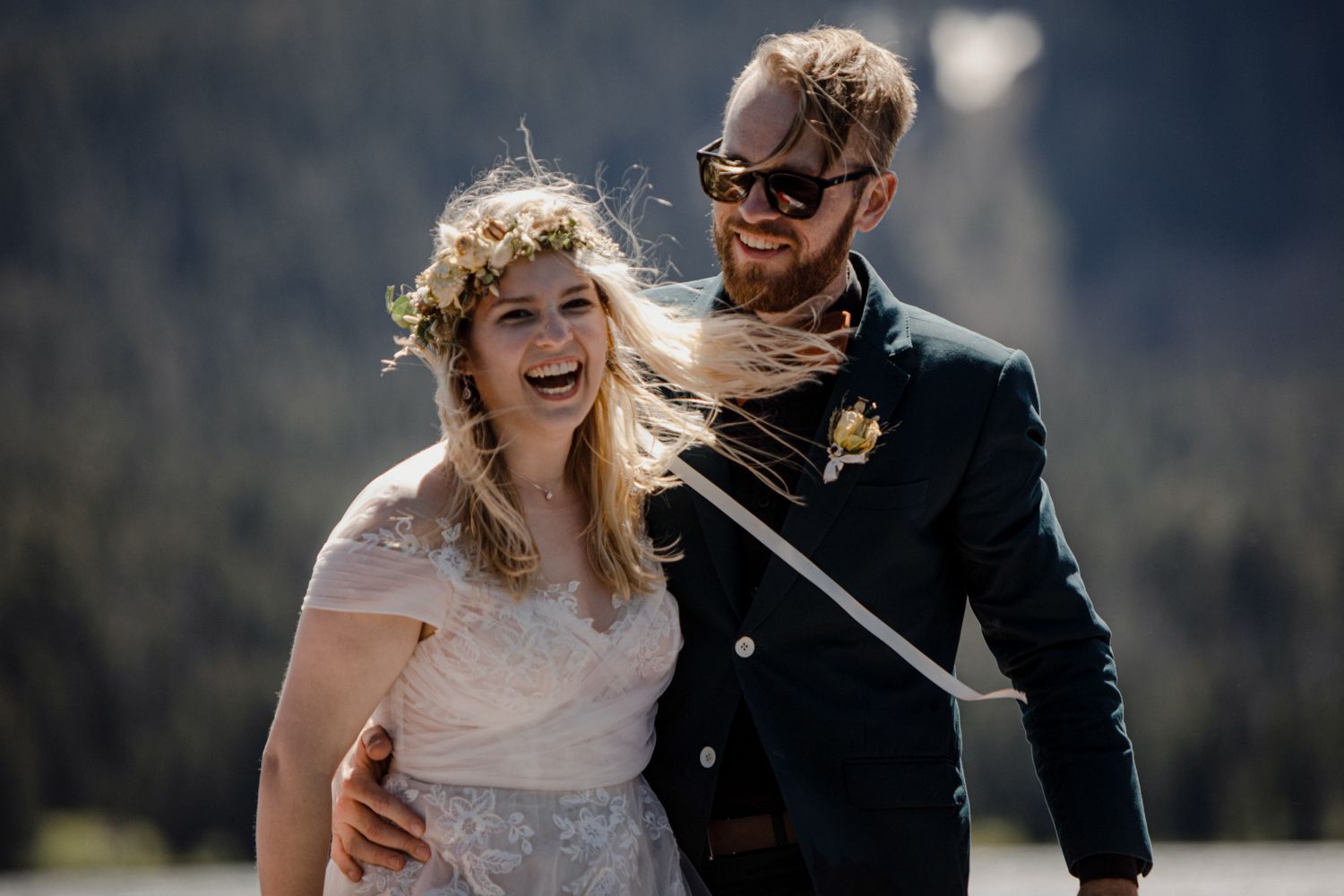 A joyful outdoor wedding scene featuring a couple in formal attire against a mountain backdrop.