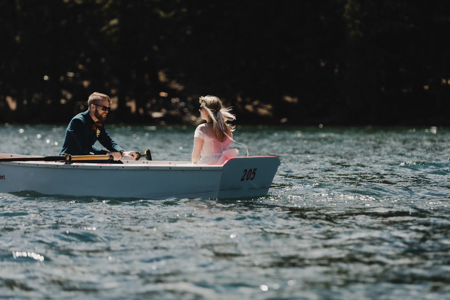 Two people rowing a small boat on a peaceful lake surrounded by forest.