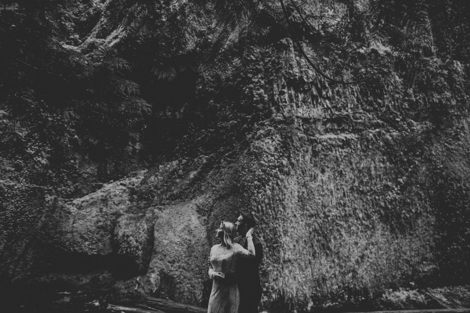 Black and white photo of a couple embracing near dramatic rock formations.