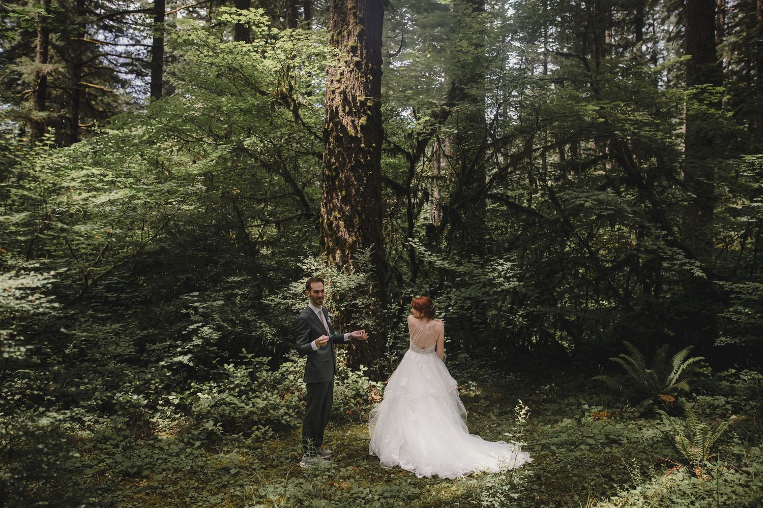 Bride and groom share a romantic moment in a lush green forest, surrounded by towering trees in a woodland wedding.