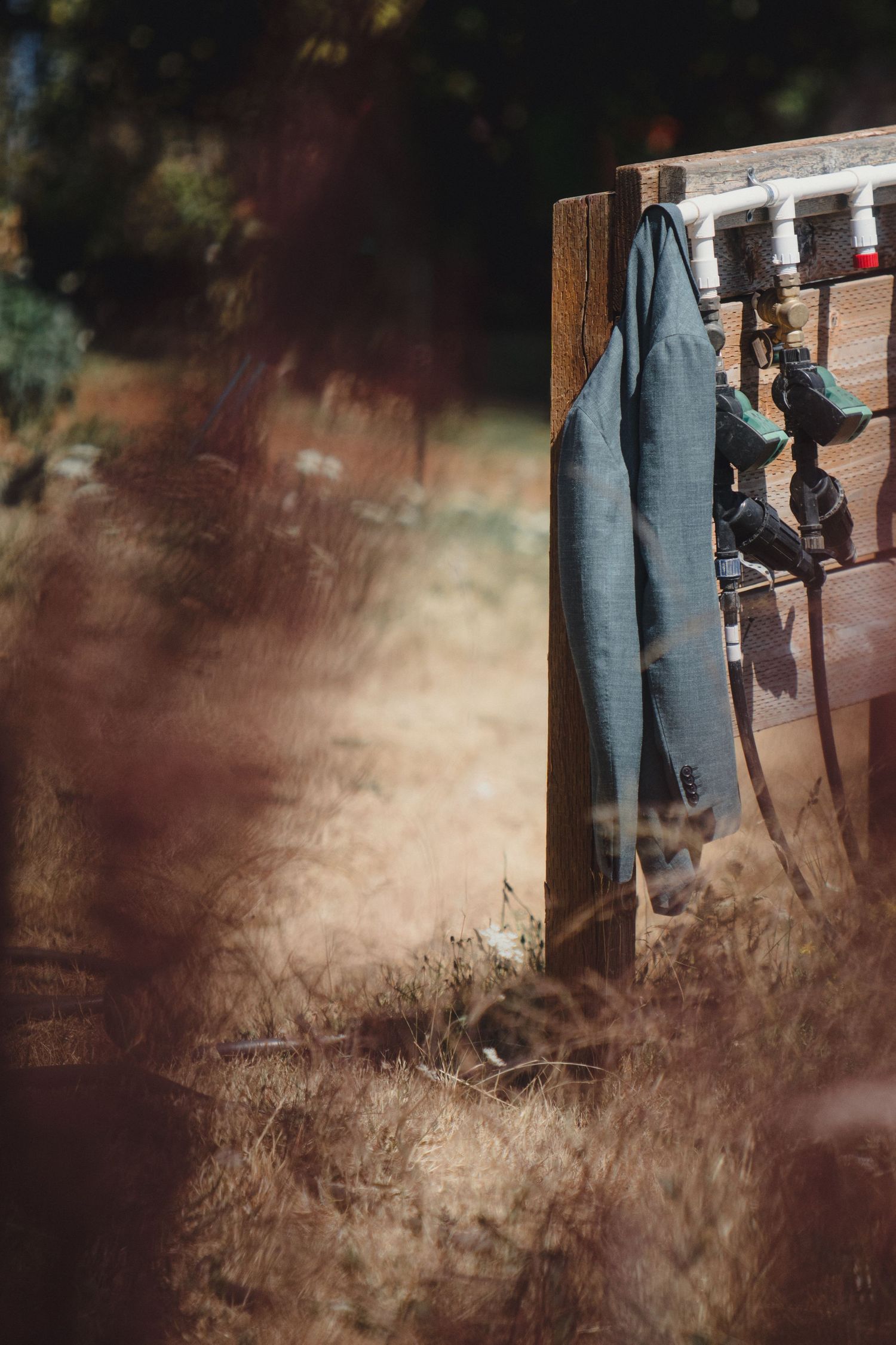 Weathered work overalls hanging on a rustic wooden post in a dry grass field.