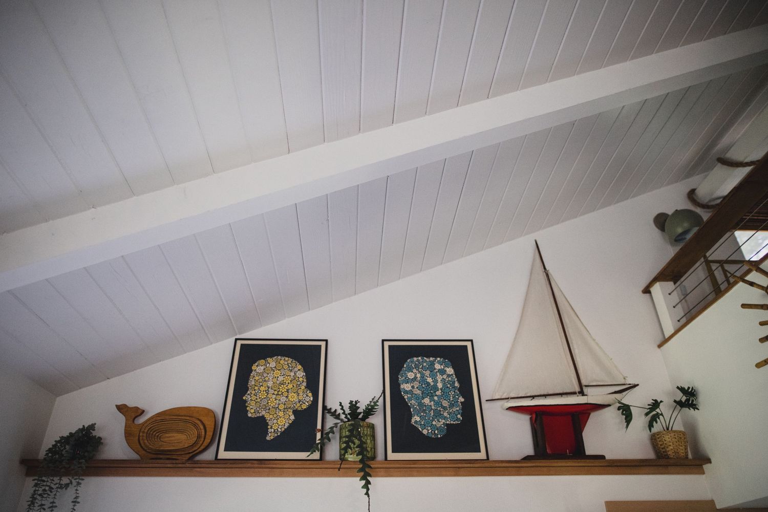 Nautical-themed interior with vaulted white ceiling, sailboat decor, and framed botanical art on shelf.