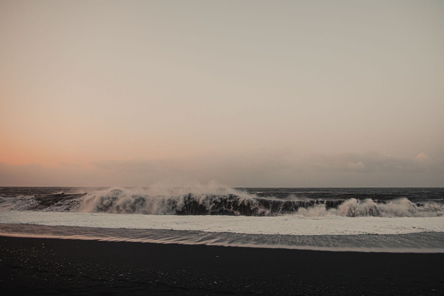 Dramatic ocean waves crash onto a black sand beach during golden hour.