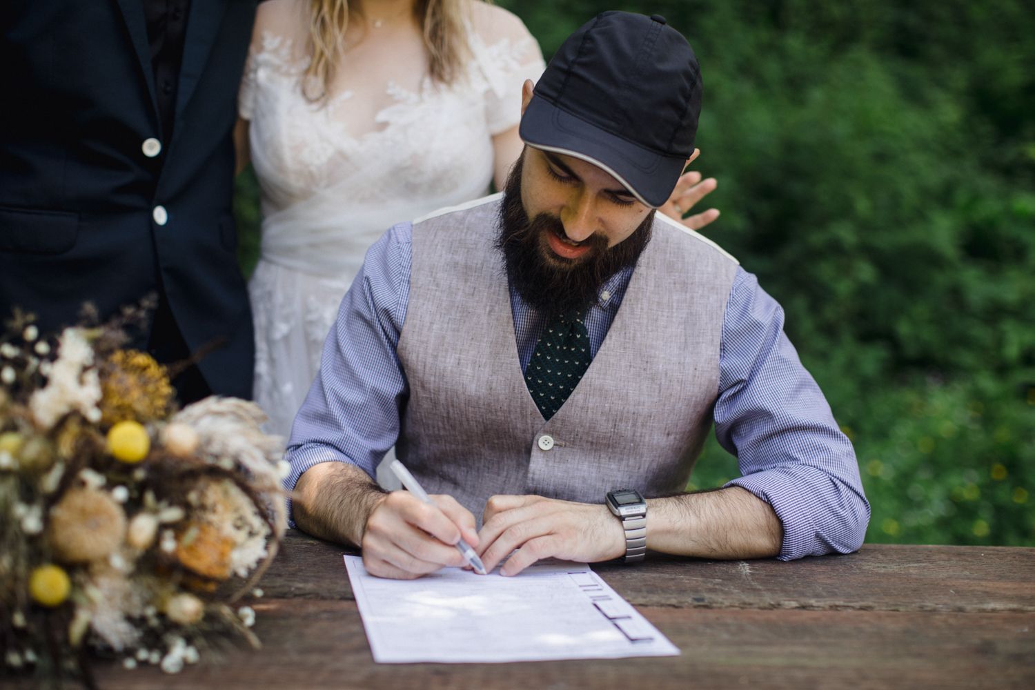 Someone signing documents on a wooden table with a flower arrangement nearby.