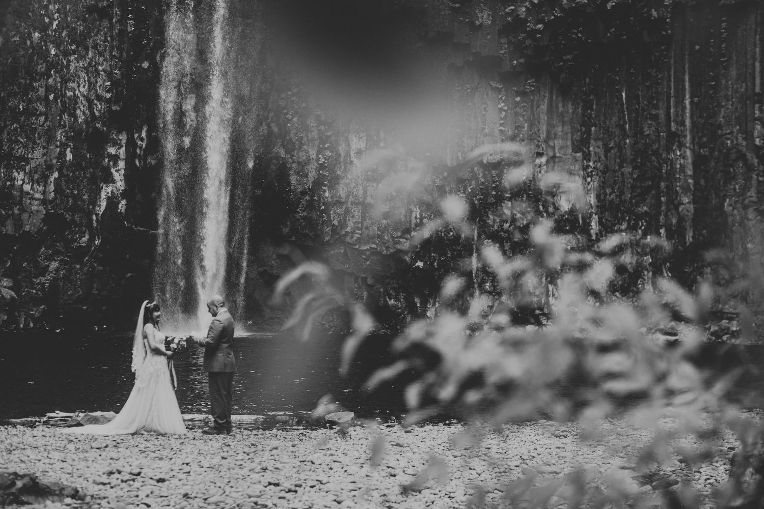 Bride and groom exchange vows in front of a stunning waterfall in a lush forest setting.
