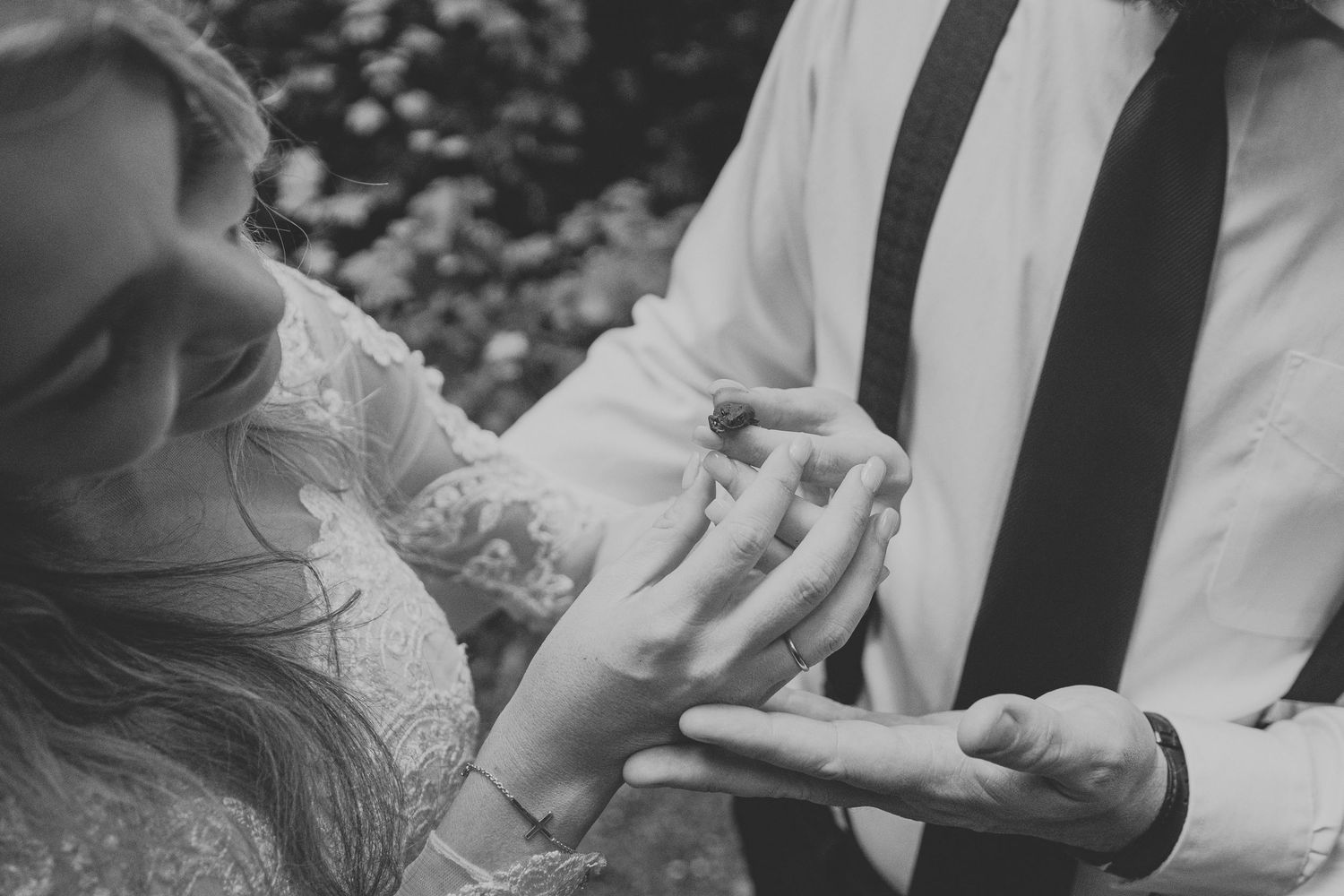 Black and white photo of bride placing wedding ring on groom's finger during romantic outdoor ceremony.