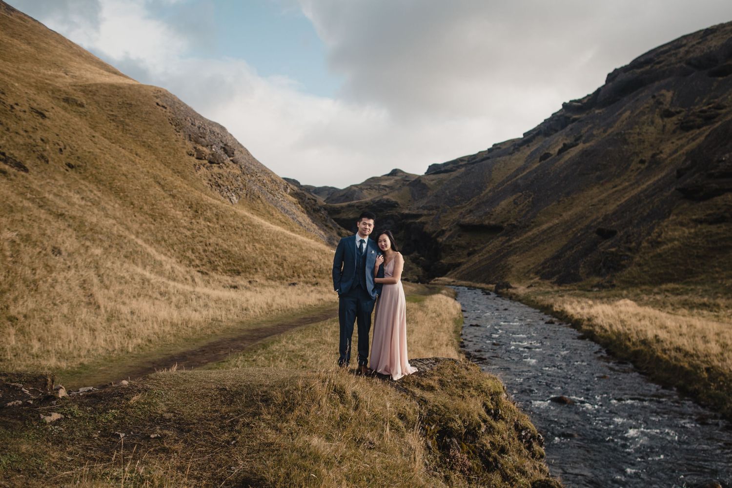 Couple standing together beside a flowing river in a scenic mountain valley.