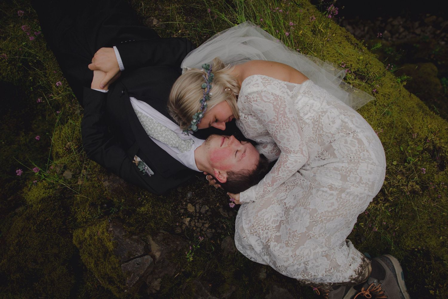 Overhead view of newlyweds sharing a joyful moment on moss-covered ground.