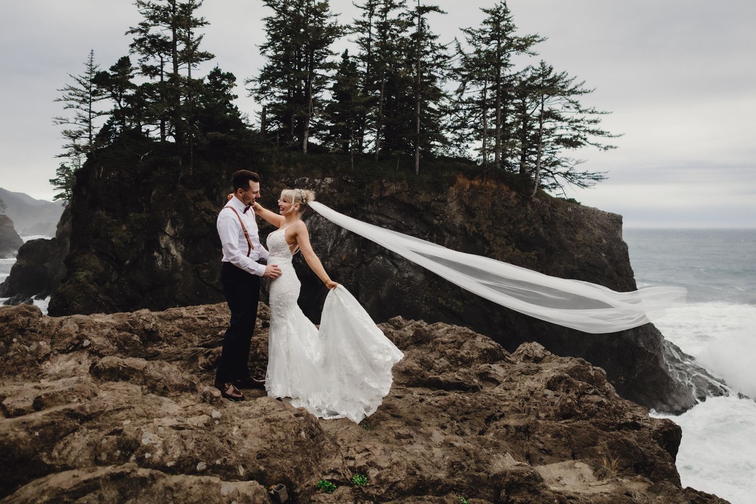 A windswept veil creates drama in this coastal cliff wedding portrait.