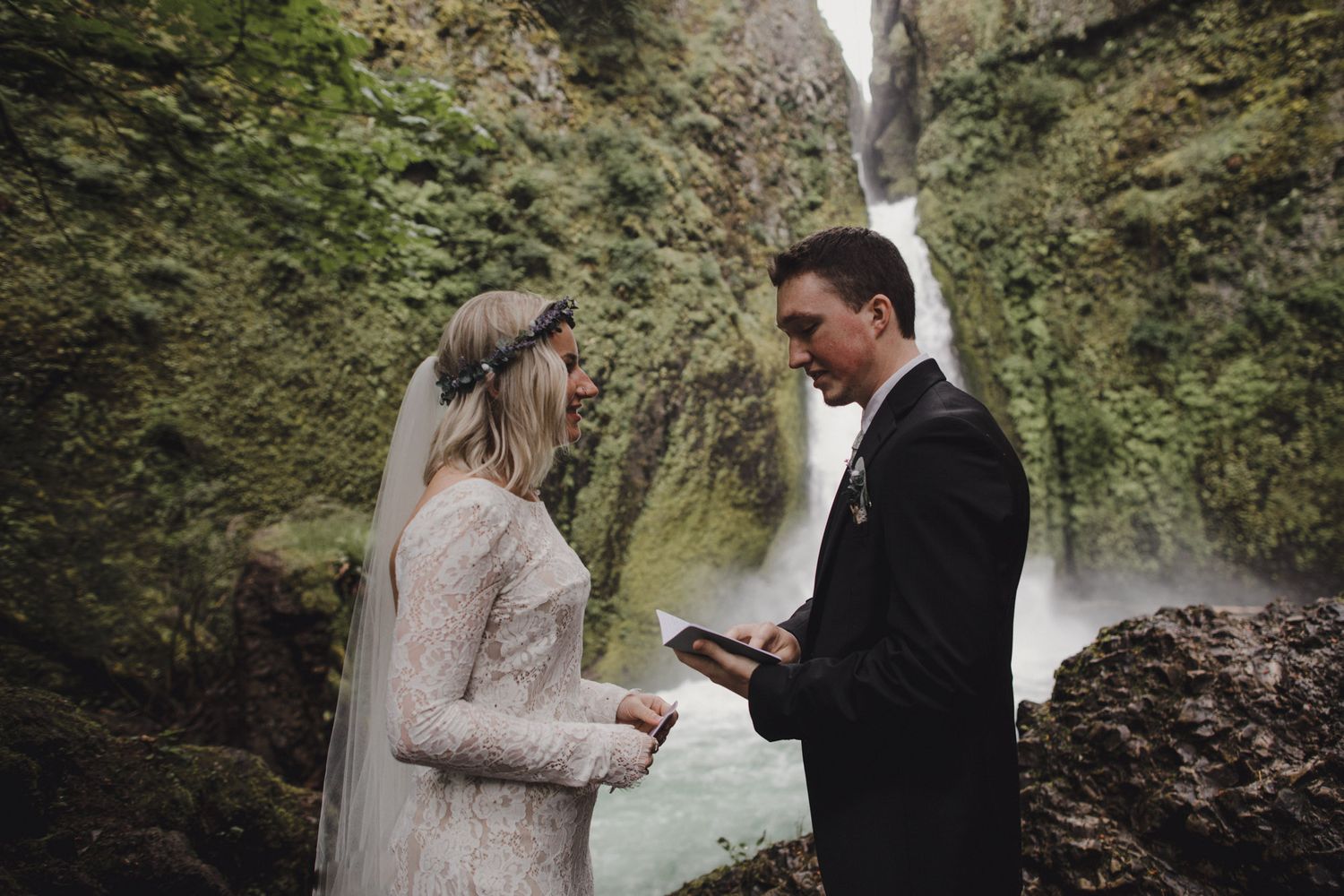 A couple exchanges wedding vows in front of a majestic waterfall surrounded by mossy green cliffs.