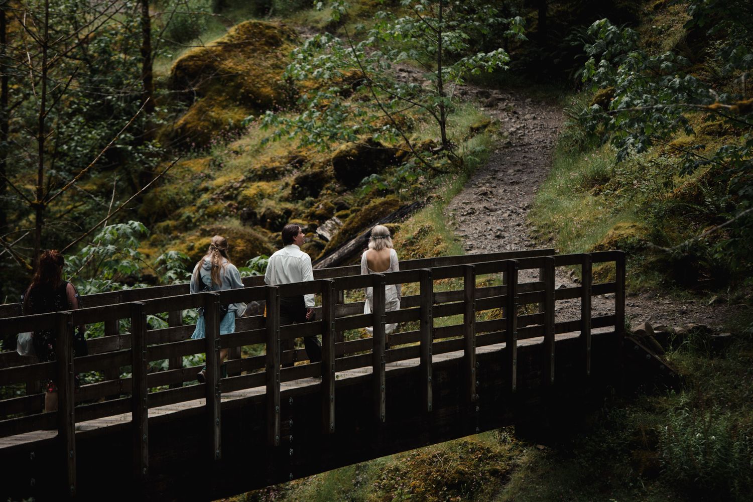 People gathered on a wooden footbridge in a lush green forest setting.