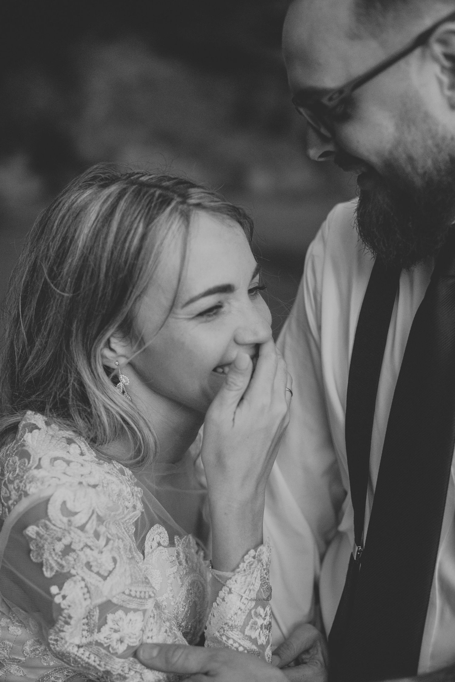 Black and white wedding photo of smiling bride in lace dress and bearded groom in suit sharing a tender moment.
